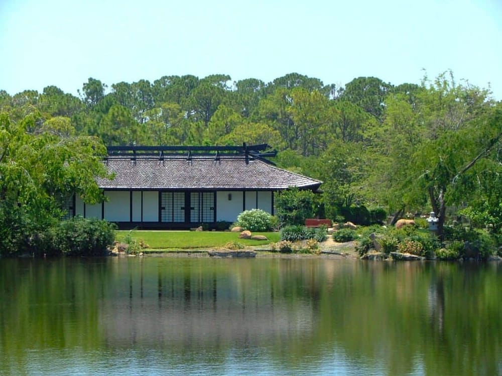 Serene Japanese-style garden with traditional pavilion by tranquil pond, lush greenery, perfect for relaxation and meditation.