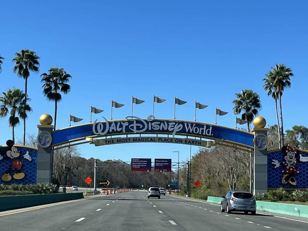 Colorful Walt Disney World entrance arch with Mickey and Minnie Mouse, palm trees, and blue sky.
