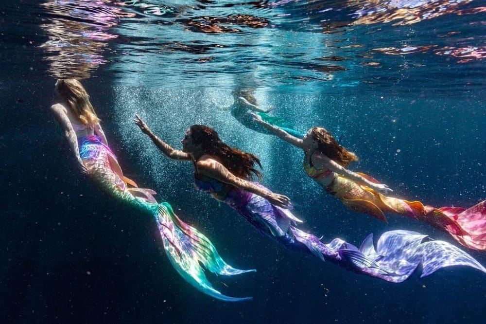 Colorful mermaids swimming underwater in an ocean scene for fantasy and myth-themed travel adventure experiences.
