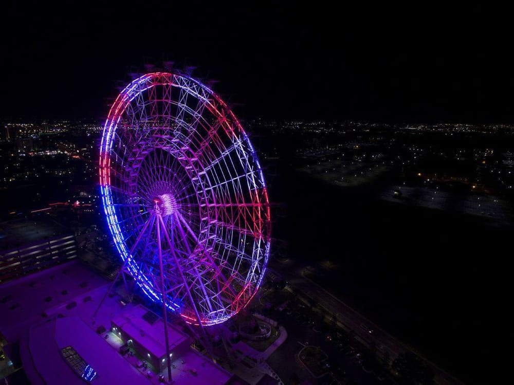 Brightly lit Ferris wheel at night with city skyline in the background, showcasing travel and entertainment attractions.