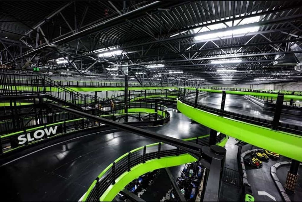 Indoor go-kart racing track with green lanes and safety barriers, modern facility with lighting and signage.