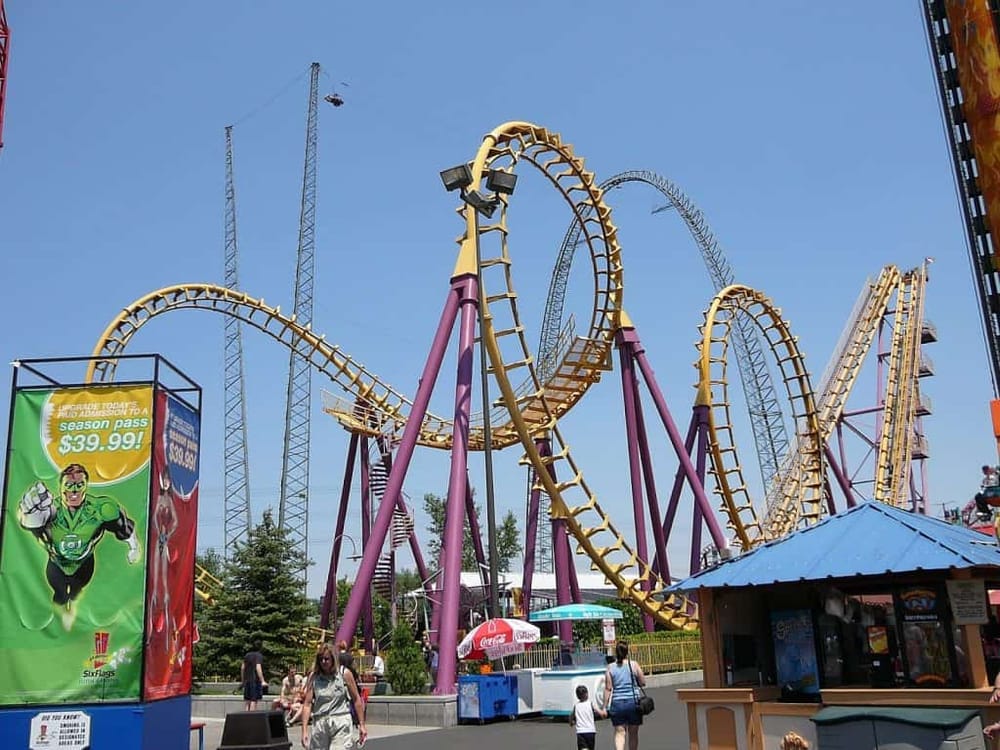 Thrilling roller coaster at Six Flags amusement park with bright yellow tracks against a clear blue sky.