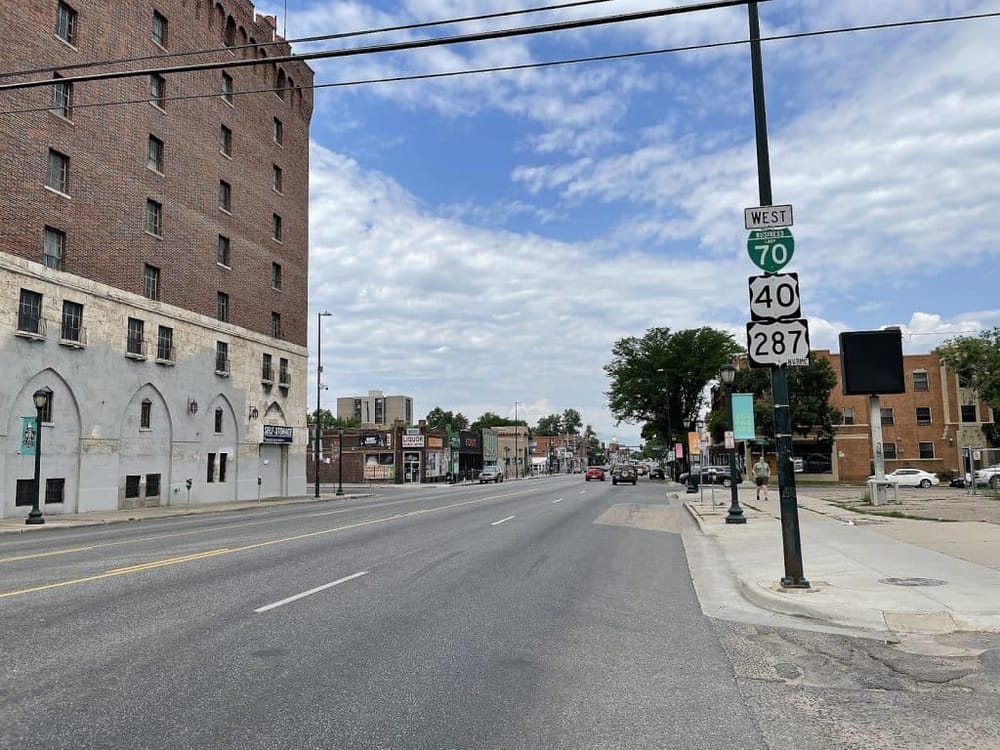 Broad Street downtown with highway signs including US Routes 70, 40, and 287, under a bright blue sky; perfect for city navigation and directions.