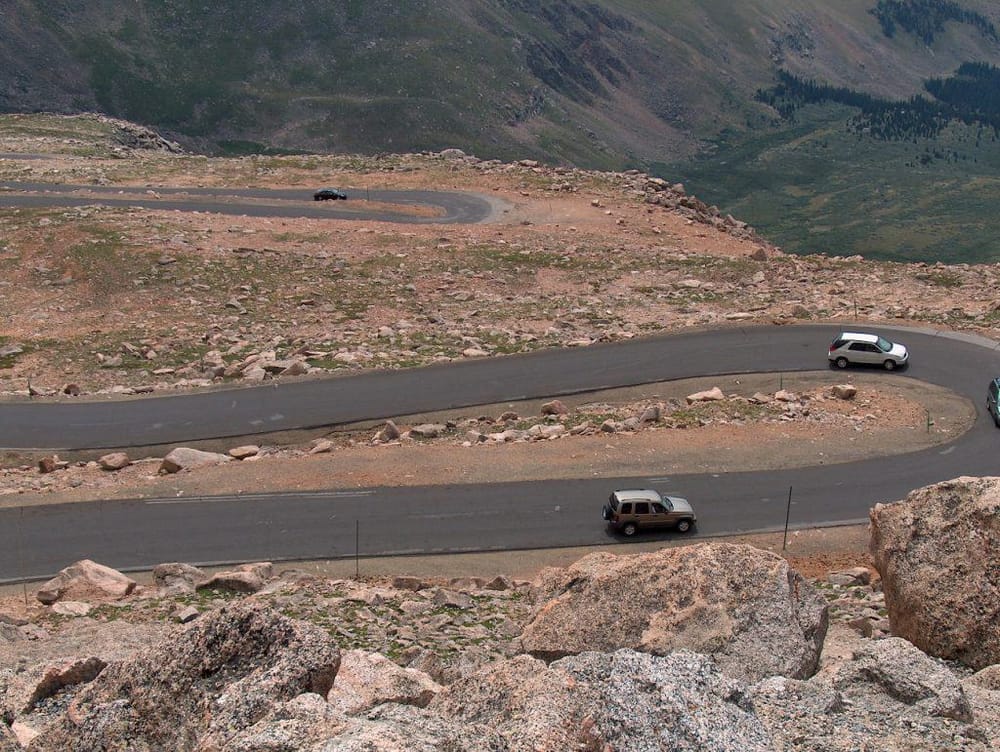 Winding mountain road with cars, scenic landscape, and rocky terrain for outdoor adventures and road trips.