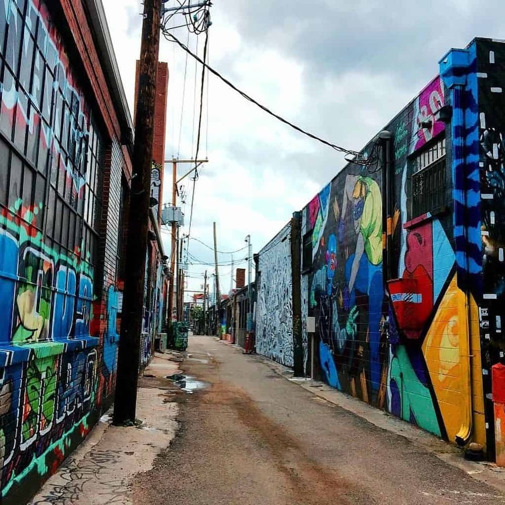 Vibrant urban alleyway with colorful graffiti murals and street art on brick walls.