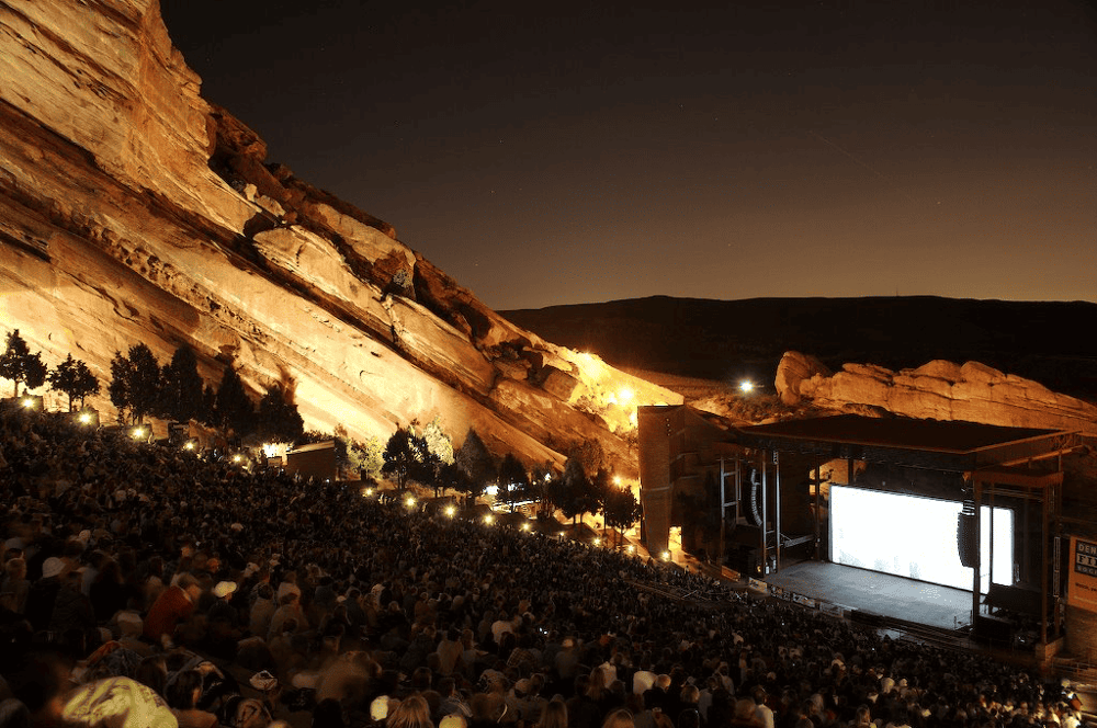Outdoor concert at Red Rocks Amphitheatre, Colorado, with illuminated rock formations and large audience.
