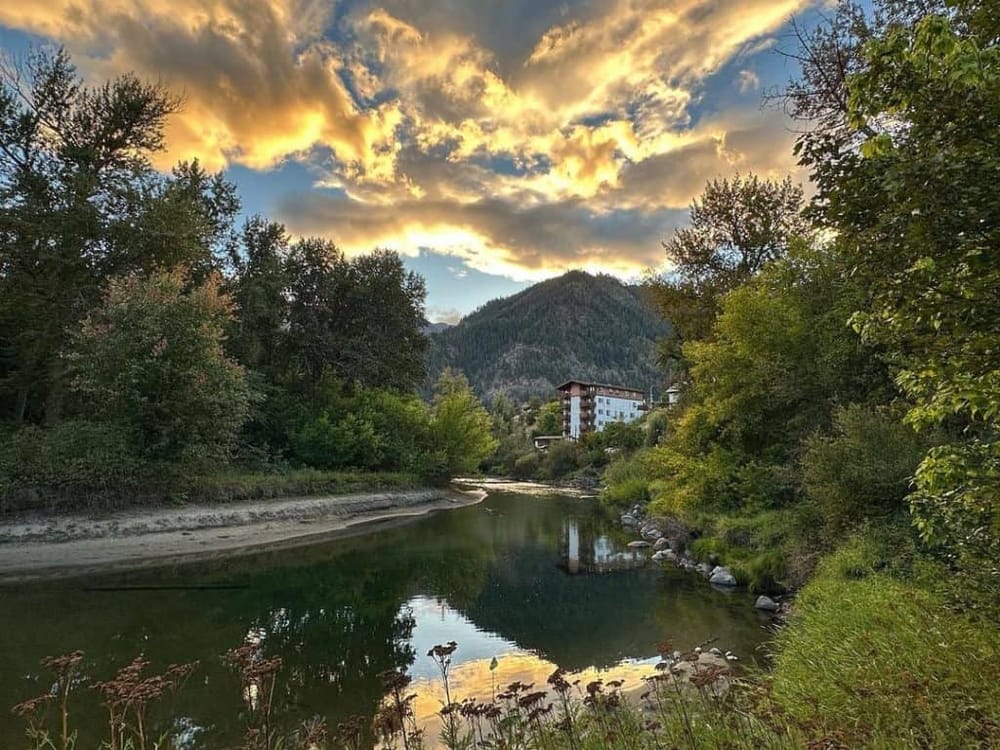 Serene mountain river with lush trees and scenic sunset in the background, perfect for outdoor adventures and nature exploration.