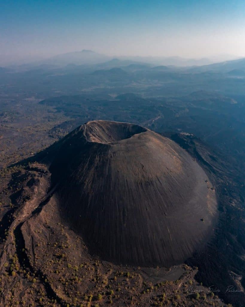 Volcano crater aerial view with volcanic landscape and distant mountains, scenic geological formation, Indonesia travel destination.