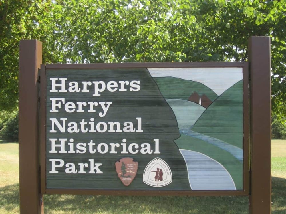 Historic Harpers Ferry National Park sign, river and mountain background, outdoor nature landscape, scenic view.