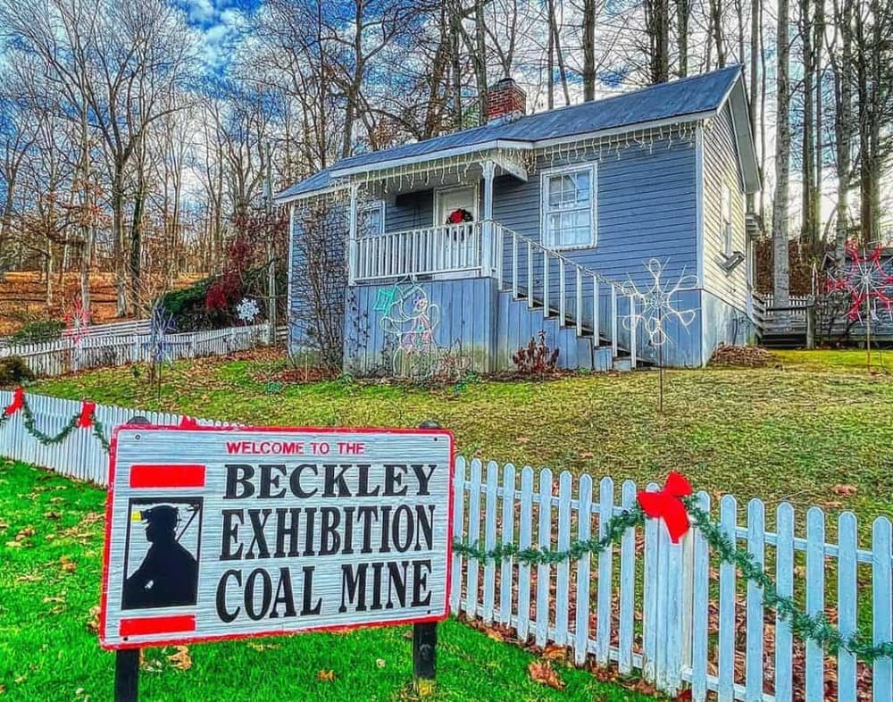 Colorful historic house decorated with holiday lights, sign for Beckley Exhibition Coal Mine, and festive fencing.