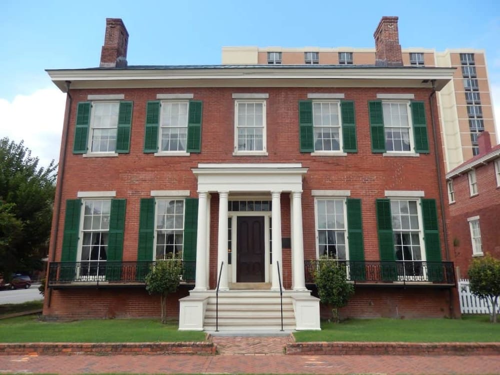Historic brick house with green shutters and classic columns, showcasing traditional architecture.