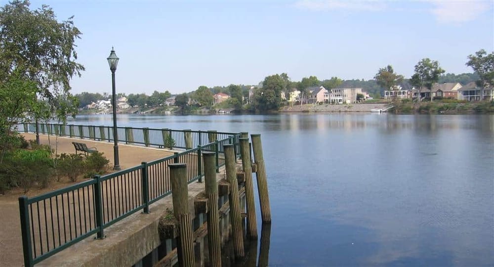 Serene riverside walkway with homes and boat docks for attractive lakeside living.