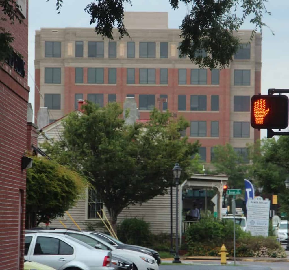 Modern cityscape with trees, cars, and a pedestrian crossing in front of a large office building.