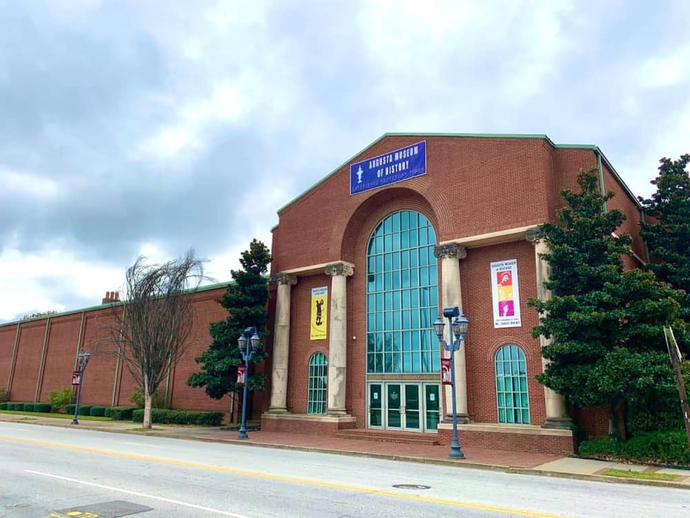 Augusta Museum of History with historic brick facade and large arched window, nestled among trees on a cloudy day.