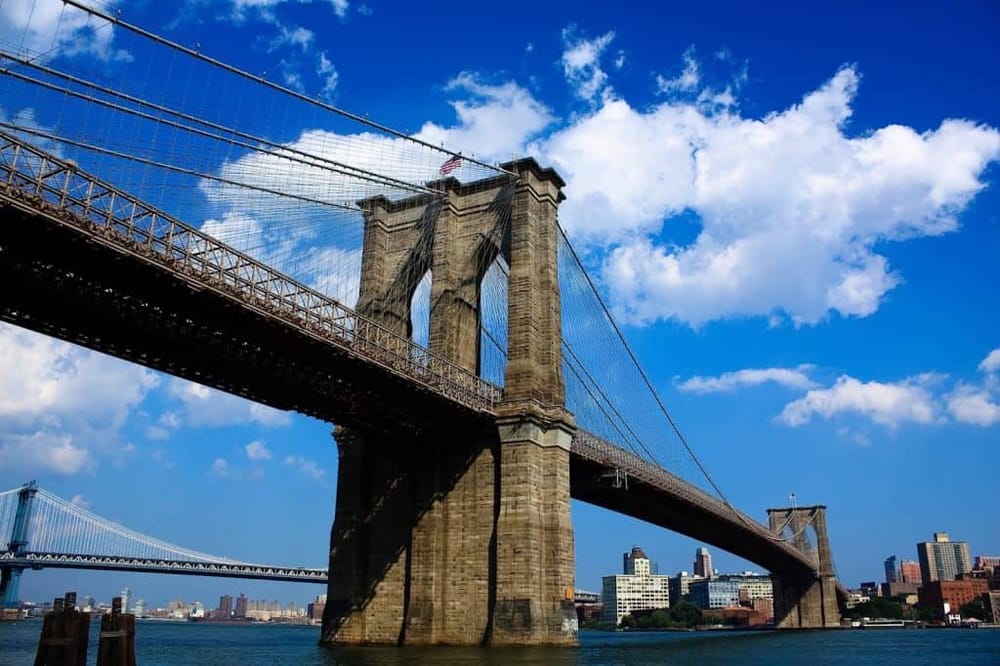 Iconic Brooklyn Bridge connecting Manhattan and Brooklyn in New York City under blue sky with clouds.