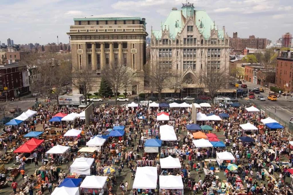 Vibrant outdoor market with tents and crowds in front of historic buildings, downtown New York City.