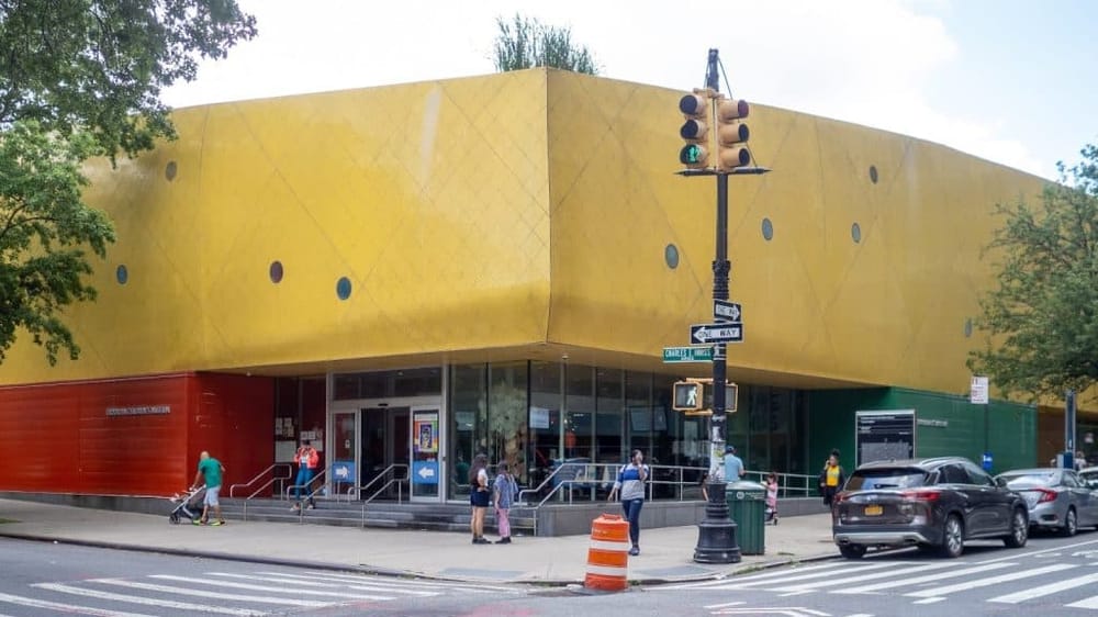 Vibrant yellow and red building with people entering and exiting, located at the intersection of Charles & 9th St in Brooklyn.
