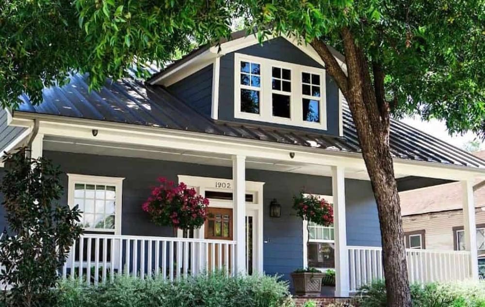 Charming blue cottage with white trim and lush greenery in a welcoming neighborhood.