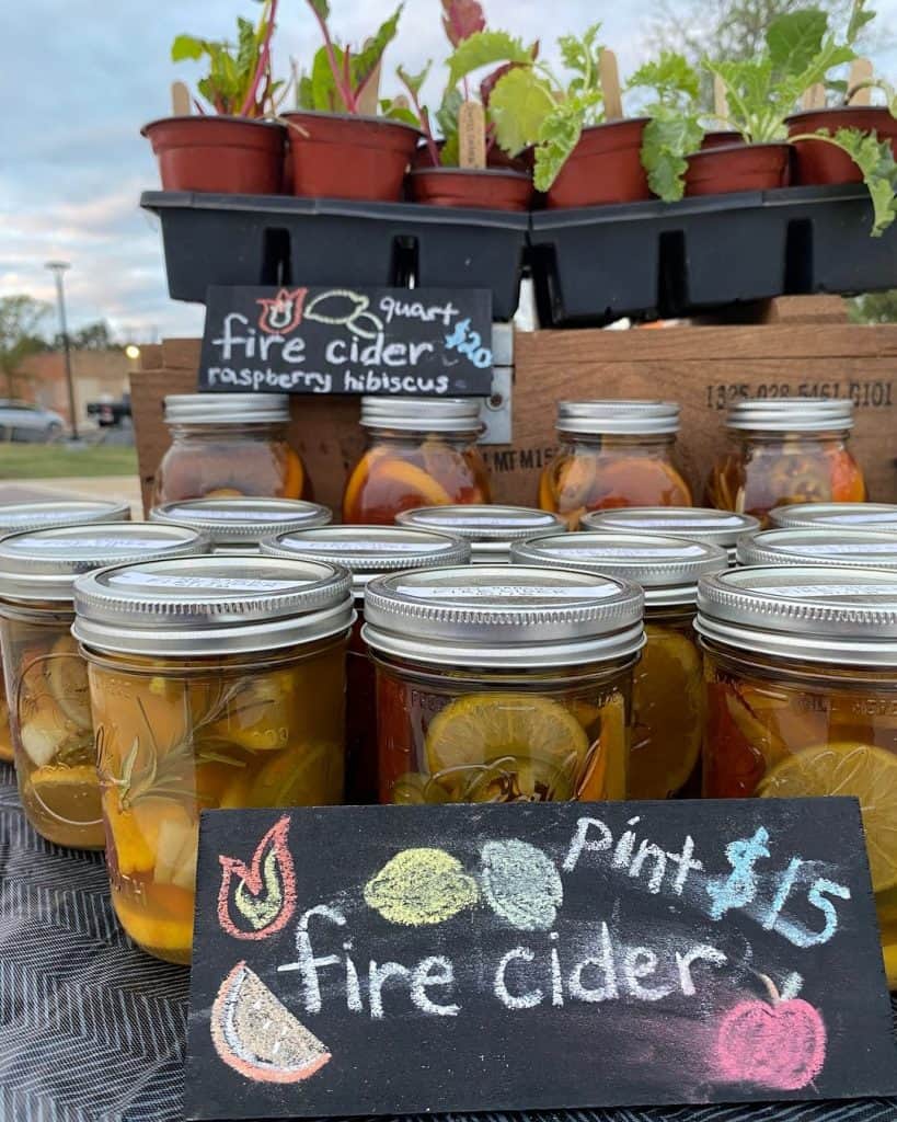 Fresh fire cider jars with lemon and fruit slices for sale at a local farmers market.