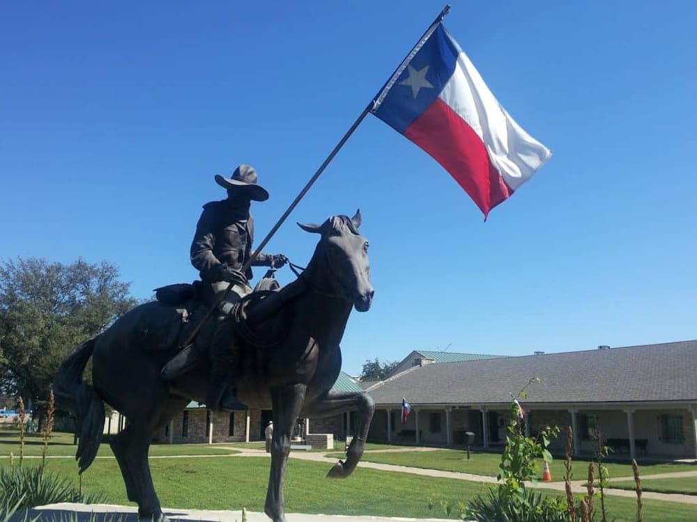 Historic Texas cowboy statue with Texas flag, outdoor landmark, travel, visit Texas, American history, outdoor decor.