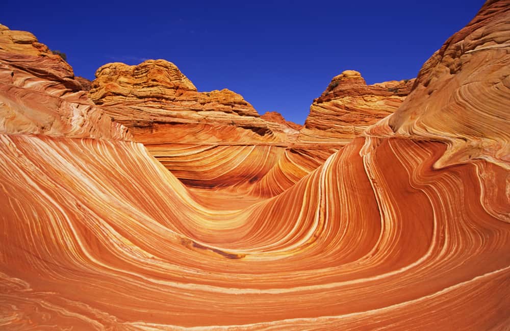 Vivid desert canyon with swirling orange and red sandstone formations under a bright blue sky.