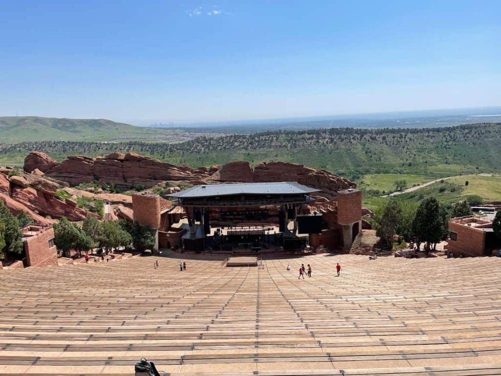 Vibrant outdoor concert venue surrounded by scenic red rocks and greenery in Colorado.