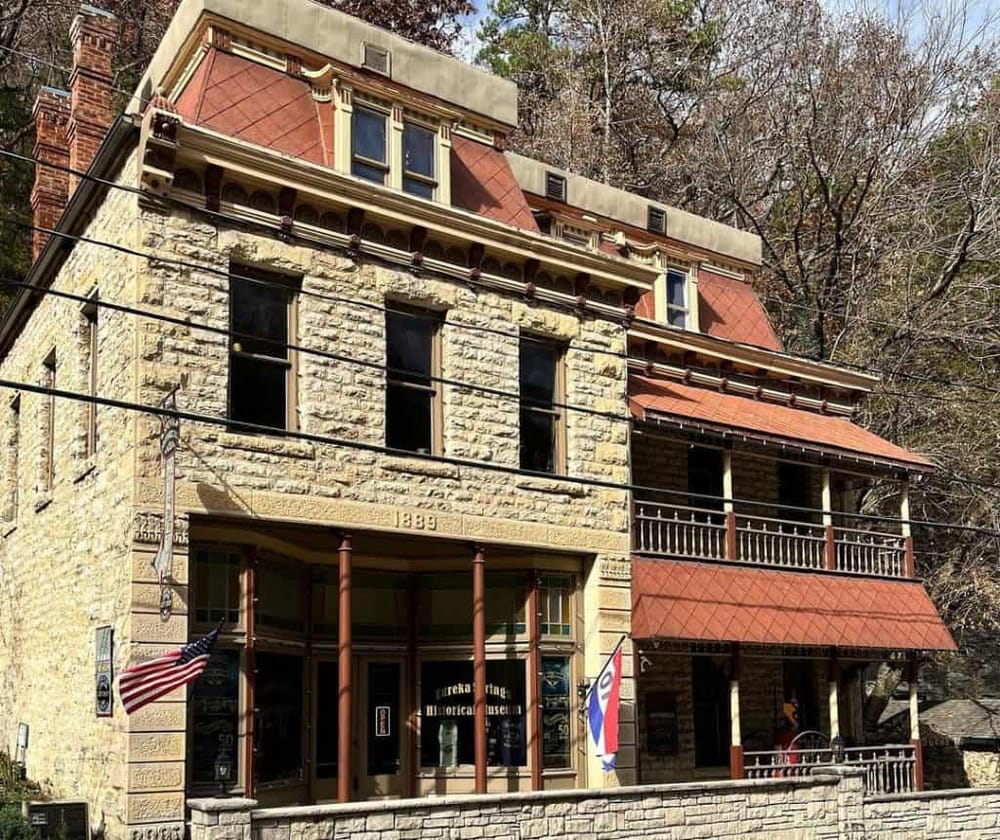 Historic Victorian building in Eureka Springs with American flags and vintage museum signage.