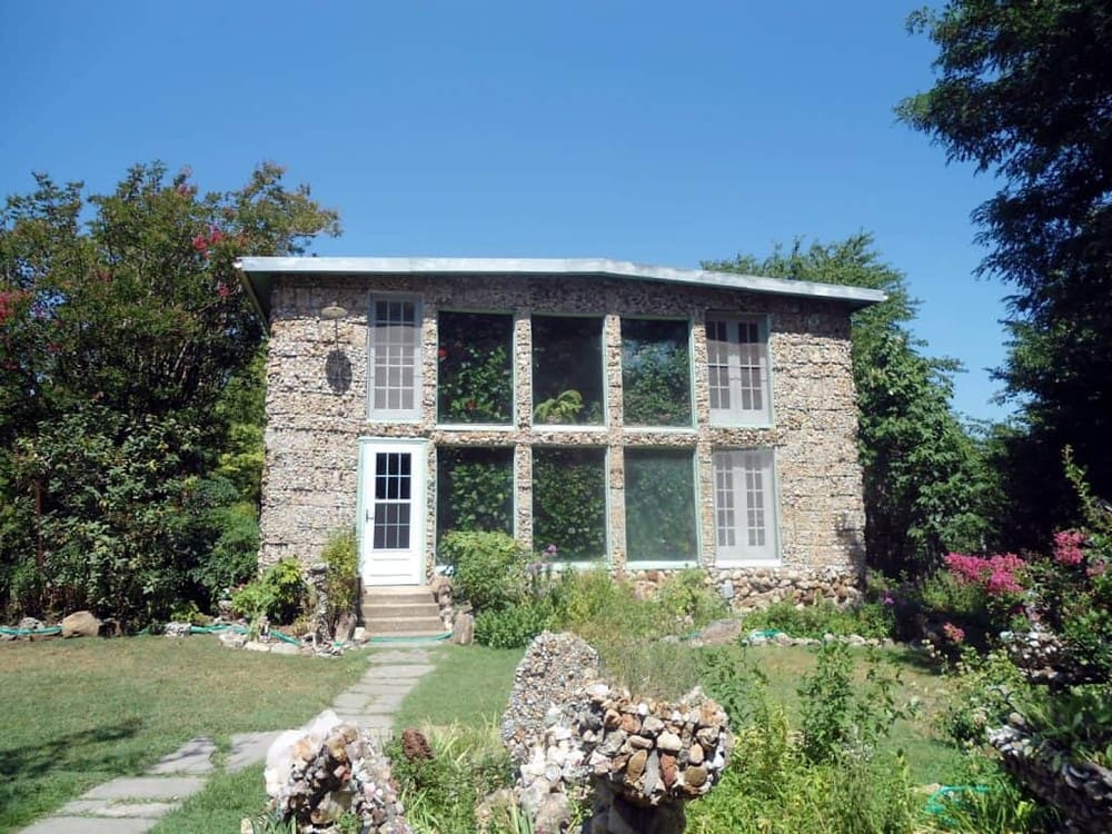 Unique stone-built eco-friendly house with large windows in a lush garden setting.