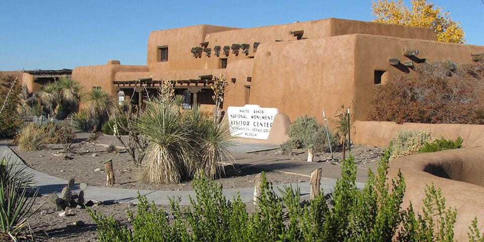 Clear desert landscape with traditional adobe architecture and native plants at the Quest for Directions site.