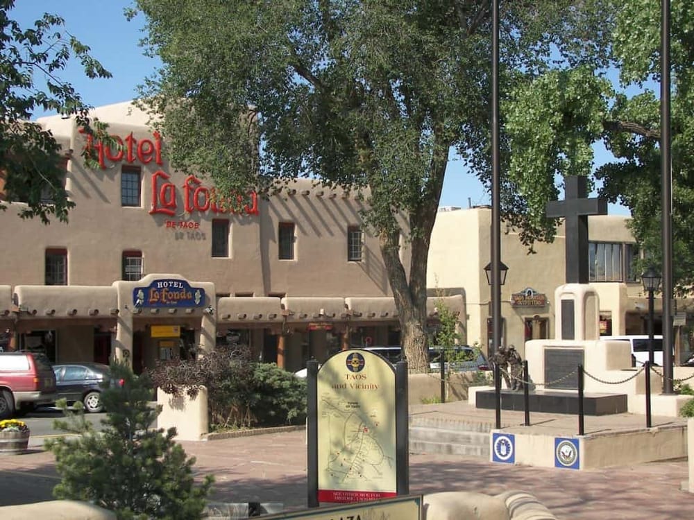 Charming Taos hotel building with signage, trees, and outdoor seating, showcasing local hospitality and cultural ambiance.
