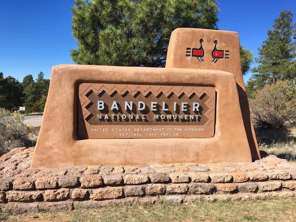 Bandelier National Monument sign at entrance, showcasing a historic outdoor park with nature and cultural heritage.