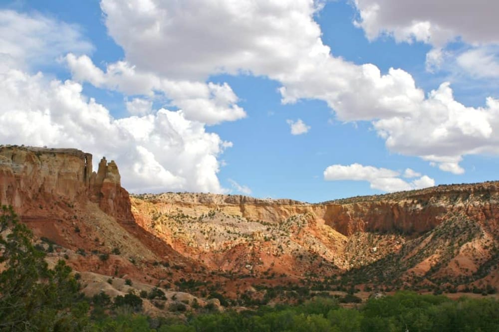 Vibrant canyon landscape with colorful rock formations and lush green vegetation under a partly cloudy sky.