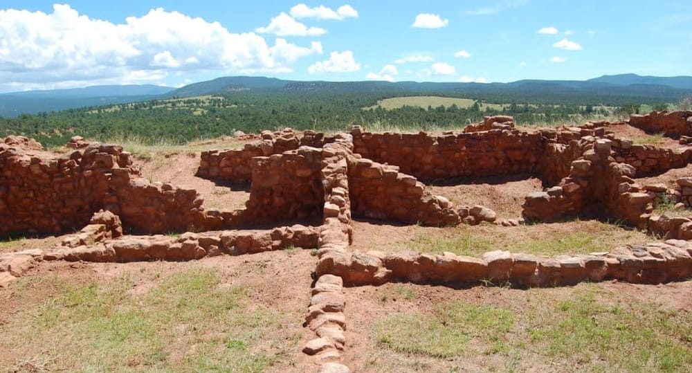 Ancient ruins of Native American archaeological site with scenic mountain views in the background.