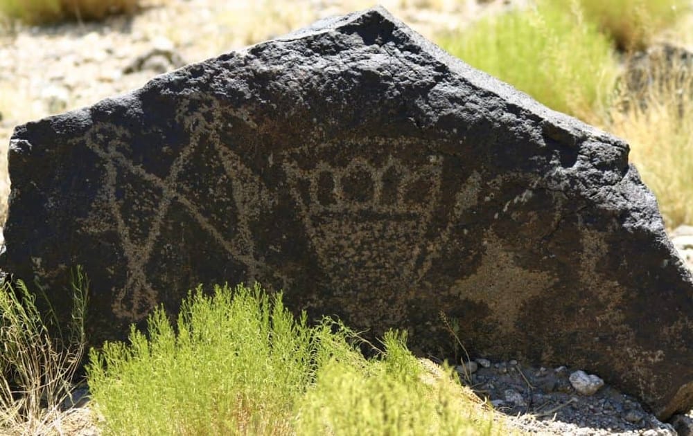 Ancient petroglyphs carved into a large rock in a desert landscape, showcasing Native American rock art.