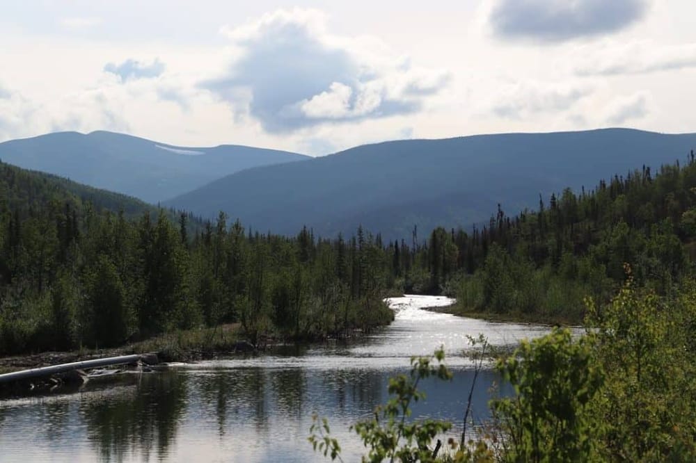 Serene river in lush green mountains during daytime, scenic outdoor landscape, perfect for nature travel and adventure.
