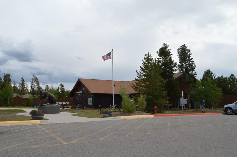 American flag outside a visitor center with forested background and bear sculpture.