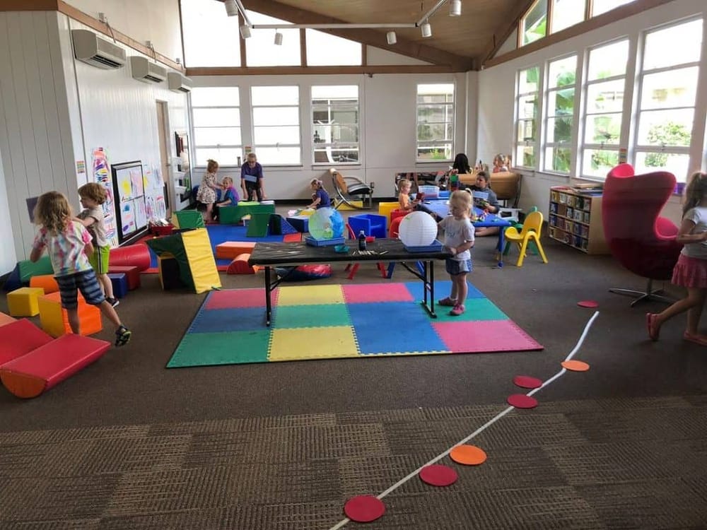 Children playing in an indoor classroom with educational toys and colorful mats.