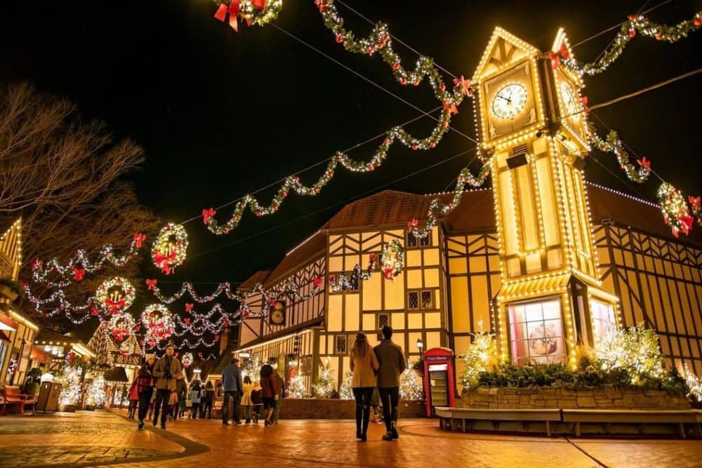Festively decorated Christmas village with illuminated clock tower at night for holiday festivities.