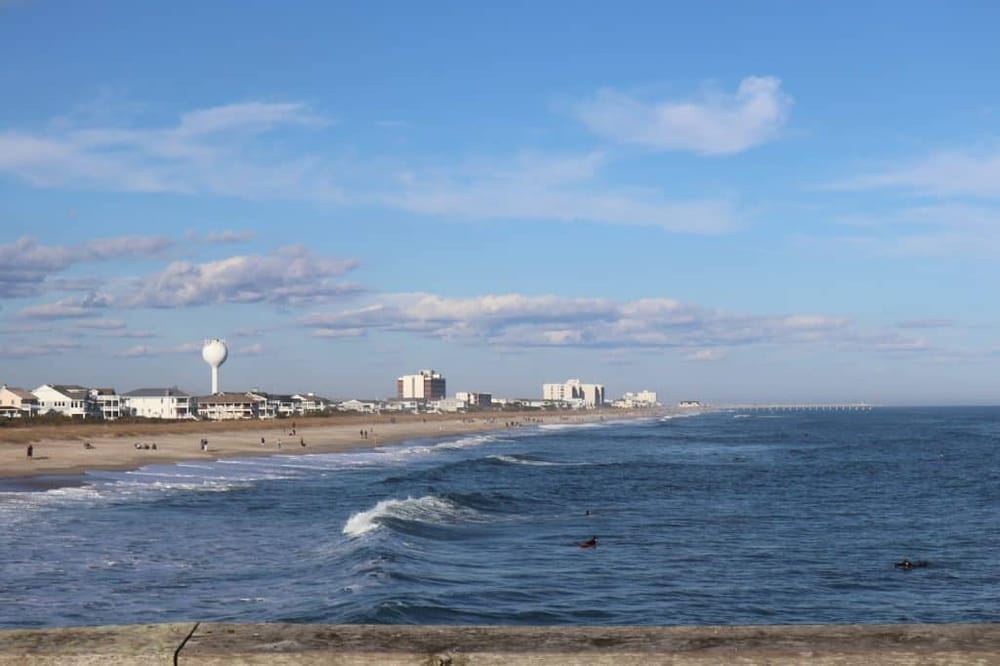 Sunny beachside in North Carolina with ocean waves and nearby coastal town scenery.