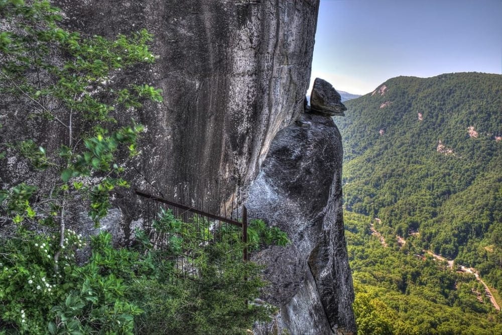 Steep mountain trail with safety railing overlooking lush green valley and rugged cliffs.