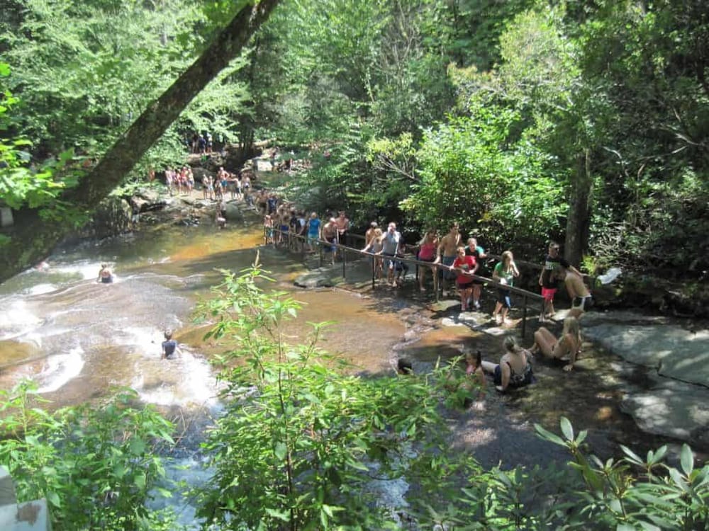 Crowd of people enjoying a scenic stream at QuestForDirections nature park, lush green forest, outdoor water activity, family-friendly destination.