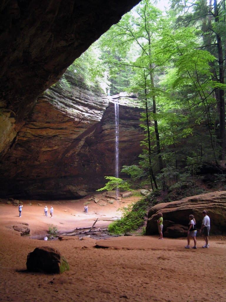 Serenity waterfall at Quest for Directions, surrounded by lush green forest, with visitors exploring the scenic canyon.