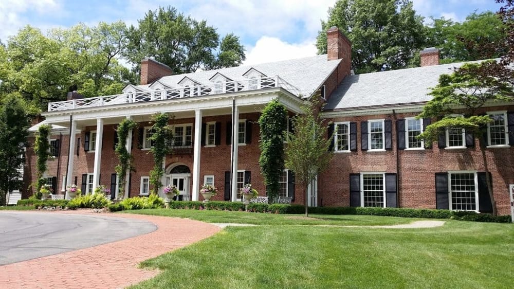 Elegant brick house with lush landscaping and a large upstairs balcony, perfect for luxurious living.