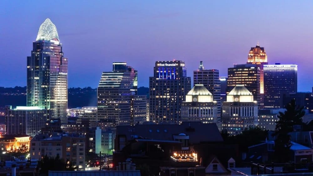 Modern city skyline with illuminated skyscrapers at dusk, featuring digital lighting and iconic buildings.