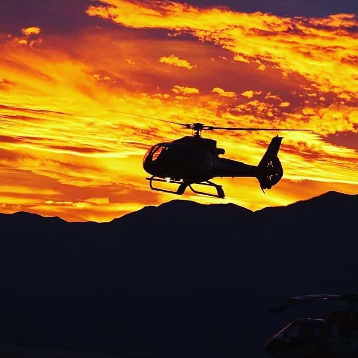 Helicopter silhouette at sunset with mountain backdrop, adventure travel, QuestForDirections.