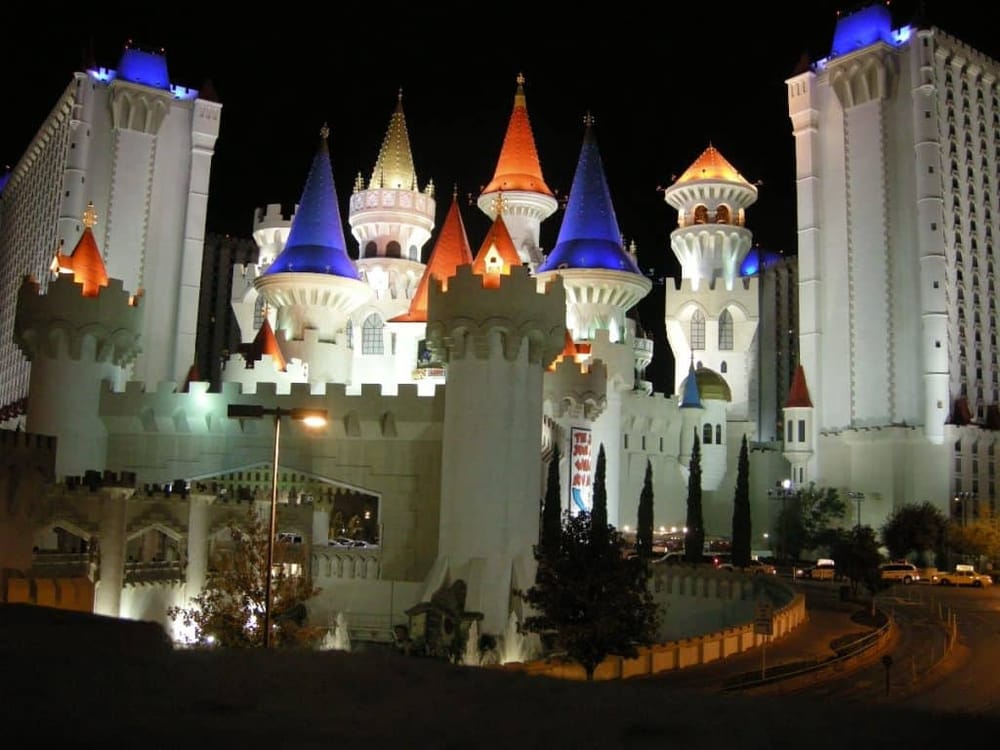 Colorful illuminated castle at night, featuring turrets with red, blue, and gold roofs.