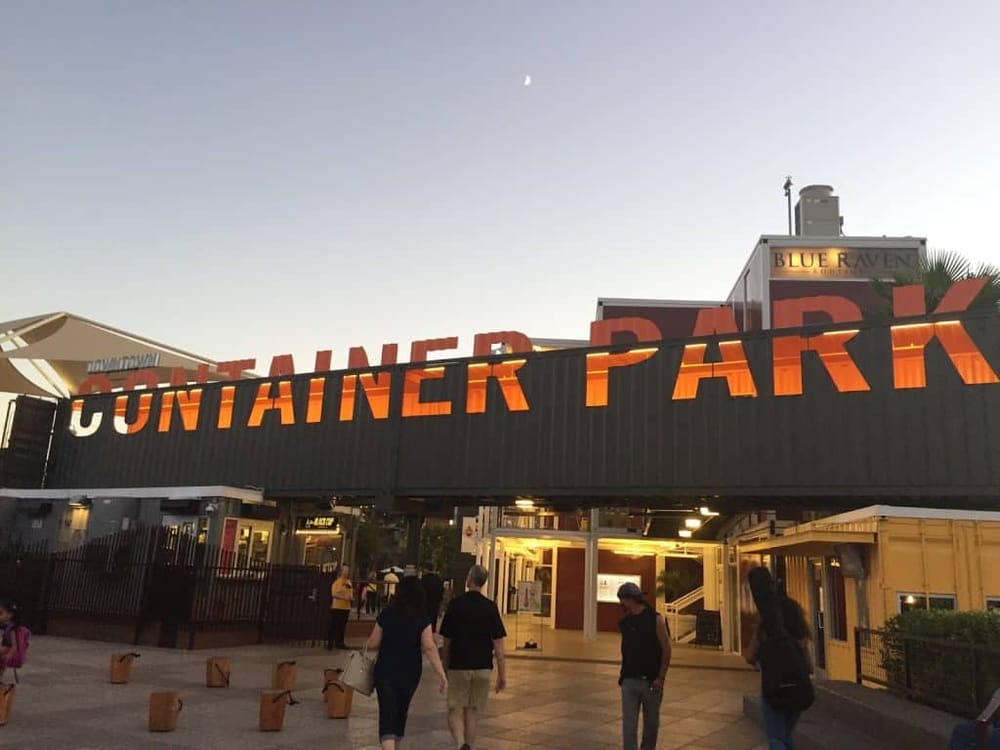 Outdoor container park at dusk featuring vibrant signage, visitors enjoying the lively atmosphere.