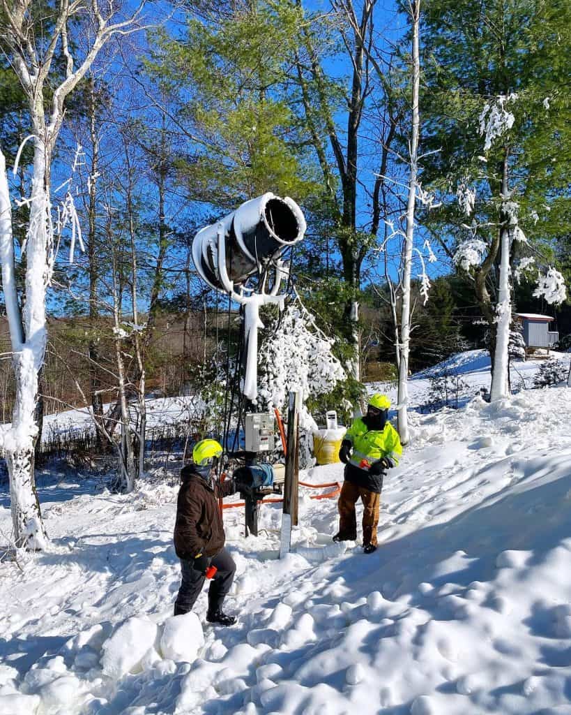 Snow-covered utility workers inspecting damaged streetlight in winter forest area.