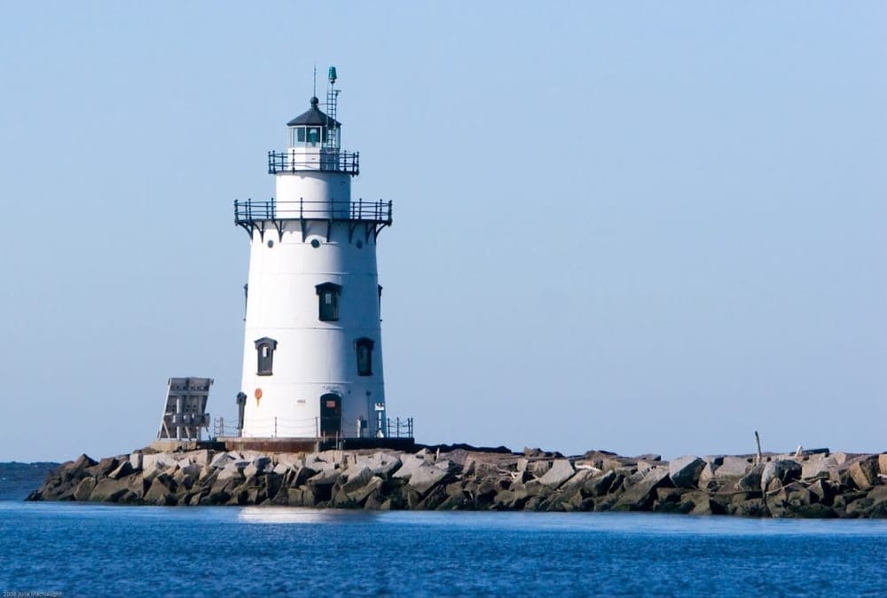 Lighthouse on rocky breakwater under clear blue sky, maritime navigation, coastal scenery.