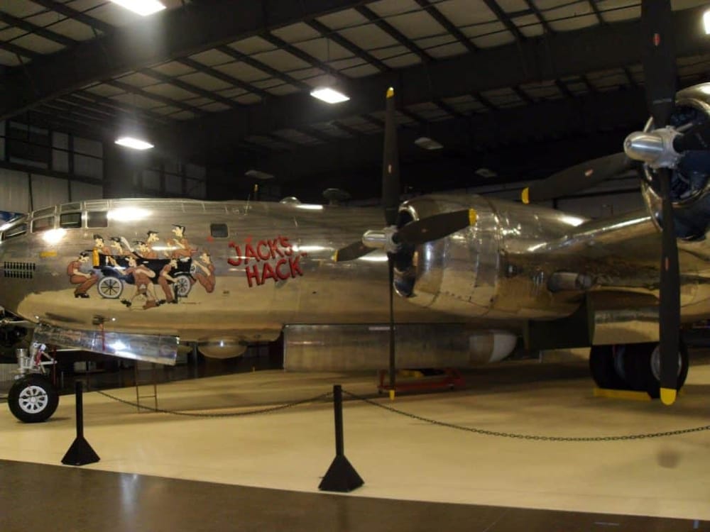 Shiny vintage bomber plane with cartoon artwork and "Jacks Hack" logo, displayed in an indoor museum.